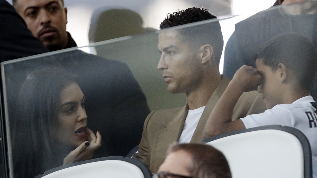 In this Oct. 2, 2018 file photo, Juventus forward Cristiano Ronaldo, centre, is flanked by his girlfriend Georgina, left, and his son Cristiano Jr, as he sits in the stands during a Champions League, group H football match against Young Boys, at the Allianz stadium in Turin, Italy. (AP Photo/Luca Bruno, File).