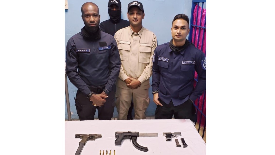 Police officer stand with three firearms and ammunition they found in Morvant.