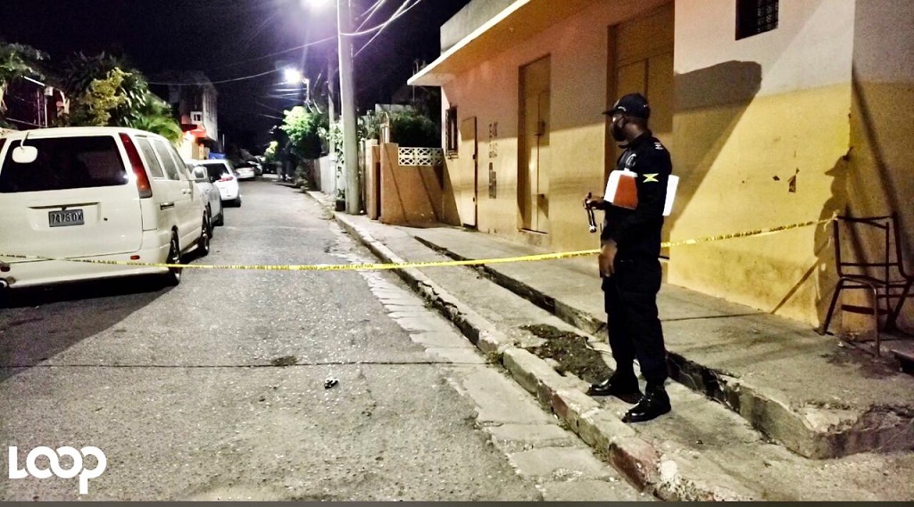 A police officer stands inside the cordoned section of the road after a triple killing in Allman Town, St Andrew on Sunday.