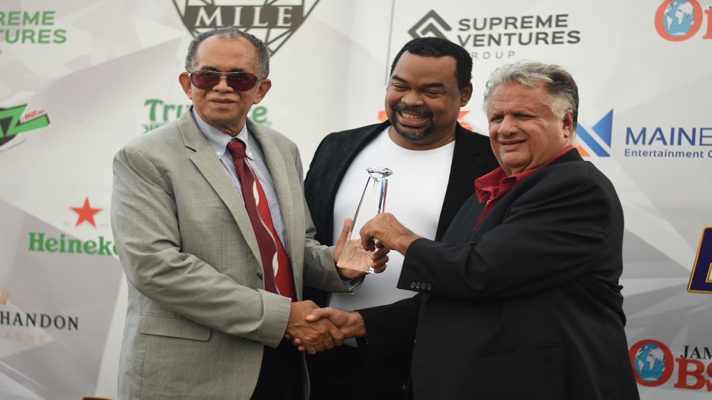 A November 9, 2019 file photo of Wayne DaCosta (right) receiving his trophy from Clovis Metcalfe, chairman of the Betting Gaming and Lotteries Commission, 
after She's A Maneater won the Diamond Mile at Caymanas Park.  Gary Peart, Chairman of Supreme Ventures Limited, shares in the occasion. (PHOTO: Marlon Reid).