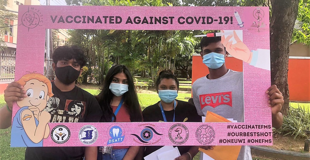 UWI圣奥古斯丁校区的学生们在UWI酒店和会议中心接种COVID-19疫苗后摆姿势拍照。