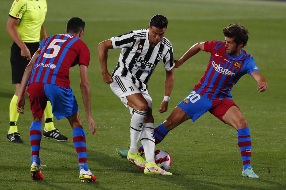Juventus' Cristiano Ronaldo, centre, tries to get past Barcelona's Sergio Busquets, left and Sergi Roberto during the Joan Gamper trophy soccer match between FC Barcelona and Juventus at the Estadi Johan Cruyff in Barcelona, Spain, Sunday, Aug. 8, 2021. (AP Photo/Joan Monfort)