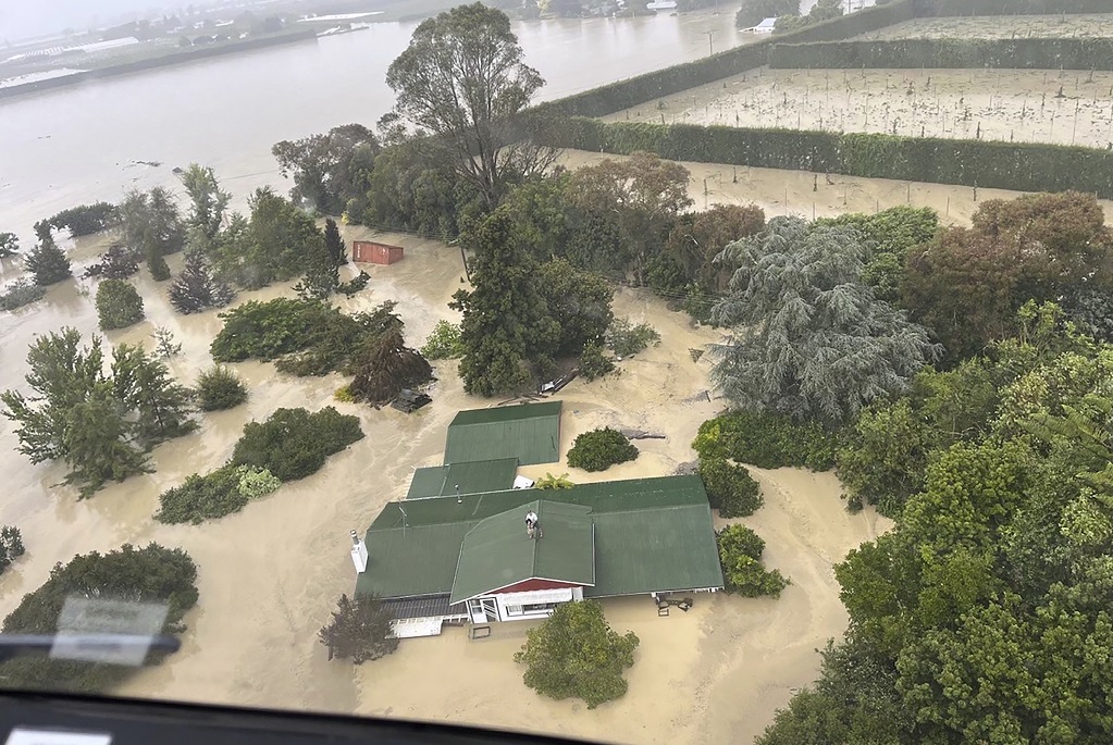 In this image released by the New Zealand Defense Force on Wednesday, February 15, 2023, people stand on a rooftop of a home waiting to be winched to safety by helicopter in the Esk Valley, near Napier, New Zealand. The New Zealand government declared a national state of emergency Tuesday after Cyclone Gabrielle battered the country's north in what officials described as the nation's most severe weather event in years. (New Zealand Defense Force via AP)