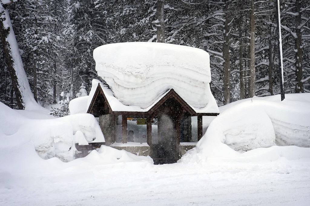 A person sits in a snow-covered bus stop Friday, February 24, 2023, in Olympic Valley, Calif. California and other parts of the West are facing heavy snow and rain from the latest winter storm to pound the United States. (AP Photo/John Locher)