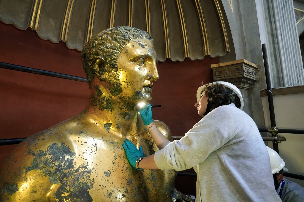 Vatican Museum restorer Alice Baltera works on the bronze Hercules statue, in the Round Hall of the Vatican Museums, Thursday, May 11, 2023. Work will continue until December to reveal the 4-metre- (13-foot-) tall Hercules, believed to have stood in ancient Rome’s Pompey Theater, to its original golden sheen. The discovery of the gilded bronze in 1864 during work on a banker’s villa near Piazza dei Fiori made global headlines. (AP Photo/Andrew Medichini)