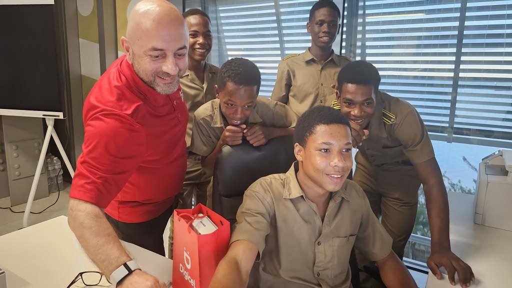 Digicel Chief Executive Officer Stephen Murad enjoys a lighthearted moment with the BB Coke High School heroes, sharing his desk with the courageous children when they visited the Digicel HQ in downtown Kingston on October 3.