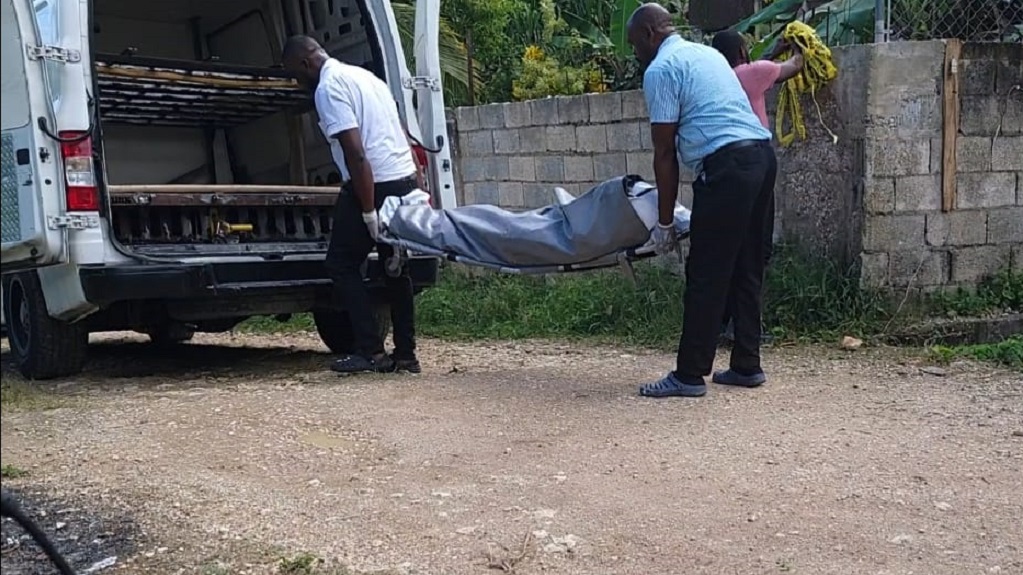 One of the bodies being removed from the crime scene in Farm View, Green Pond, St James on Saturday after two men were killed at their home.