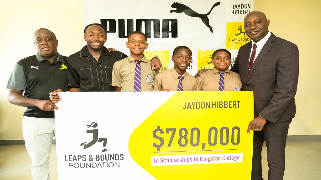 Jamaica's triple jump star sensation, Jaydon Hibbert (second from left), and Kingston College's (KC) principal Dave Myrie (right) display a symbolic check of $780,000 along with three of the five scholarship recipients at a recent handover at KC. The recipients present are Ricadeen Wilkins (third from left), Jehu Green (fourth from left), and Joshua Lewin (fifth from left). At the left is Hibbert's mentor, Ricky Martin. (PHOTO: Contributed).