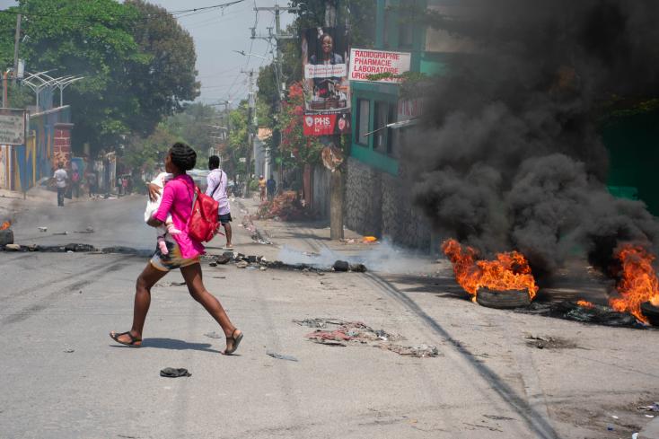 A woman, a child in her arms, runs for shelter during gunfire from armed gangs, on March 20, 2024 in Port-au-Prince, Haiti CLARENS SIFFROY / AFP  