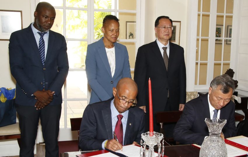 Permanent Secretary, Andrew Gittens, and Director General of the Foreign Affairs Office, Hunan Provincial People’s Government, Xu Zhengxian signing the Handover Agreement for donating solar lamps while officials look on. (Photo credit: GIS)