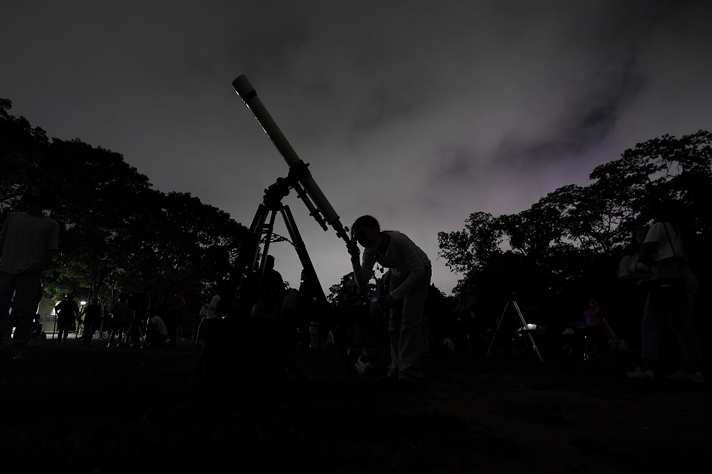 FILE - A girl looks at the moon through a telescope in Caracas, Venezuela, Sunday, May 15, 2022. Six planets will line up in the early morning sky on June 3, 2024, but most will not be visible to the eye naked.  A planetary parade occurs relatively often when several planets align on the right side of the sun, making them visible through a narrow band of our sky.  (AP Photo/Matias Delacroix)