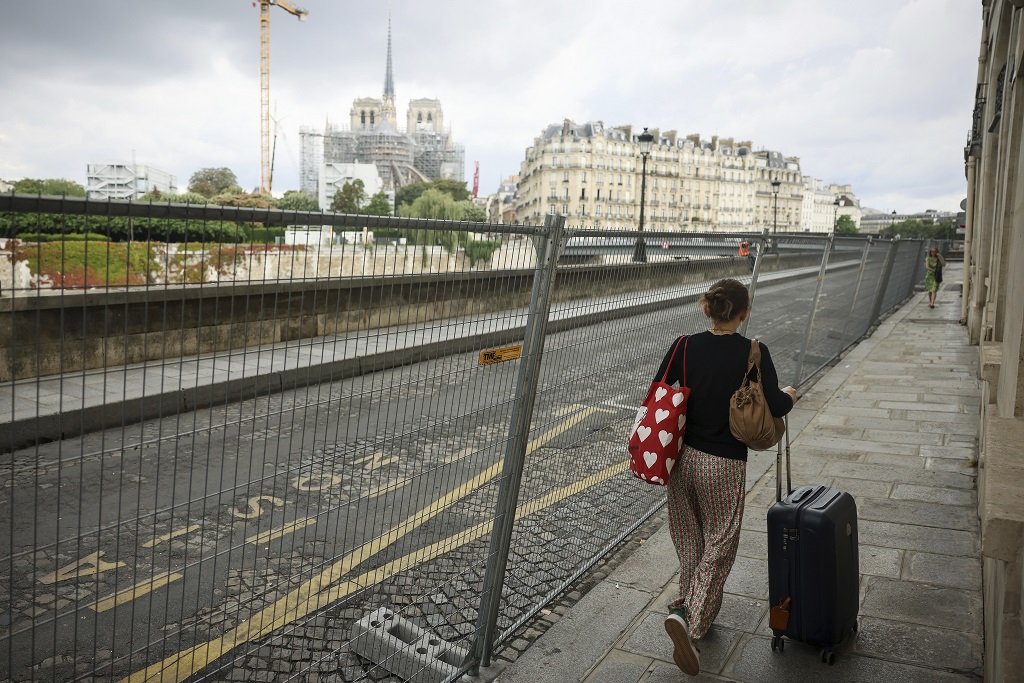 FILE - A woman pulls her luggage along fences of the security perimeter, with Notre Dame cathedral in background, at the 2024 Summer Olympics, Sunday, July 21, 2024, in Paris, France. French prosecutors are investigating an alleged rape of an Australian woman visiting Paris, just two days before the start of the 2024 Olympics. (AP Photo/Thomas Padilla, File)