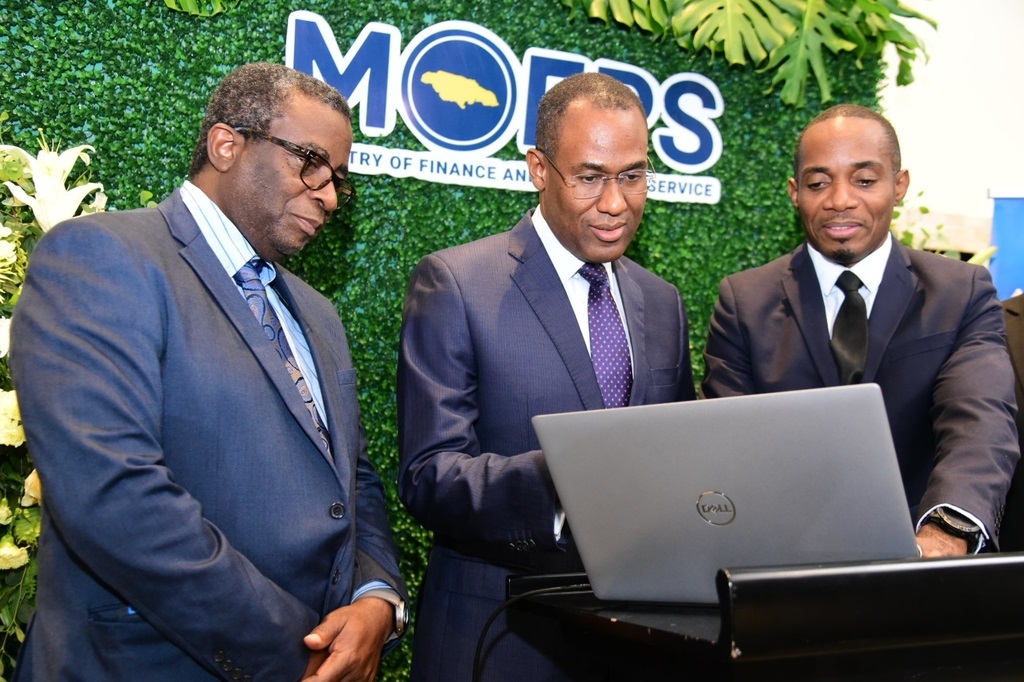 Minister of Finance and the Public Service, Dr. the Hon. Nigel Clarke (centre) and Tax Administration Jamaica (TAJ) Commissioner General, Ainsley Powell (left), observe a demonstration of the Reverse Income Tax Credit application platform by Business Requirement Specialist at the TAJ, Ricardo Campbell. The occasion was the launch of the initiative at The Jamaica Pegasus Hotel in New Kingston on Wednesday (October 2).