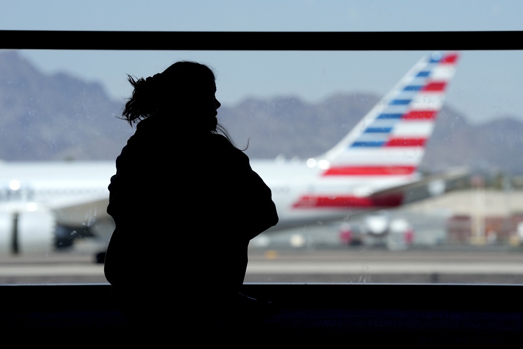 FILE - A woman waits for her flight as an American Airlines jet passes by at Sky Harbor airport on March 4, 2023, in Phoenix. (AP Photo/Charlie Riedel, File)
