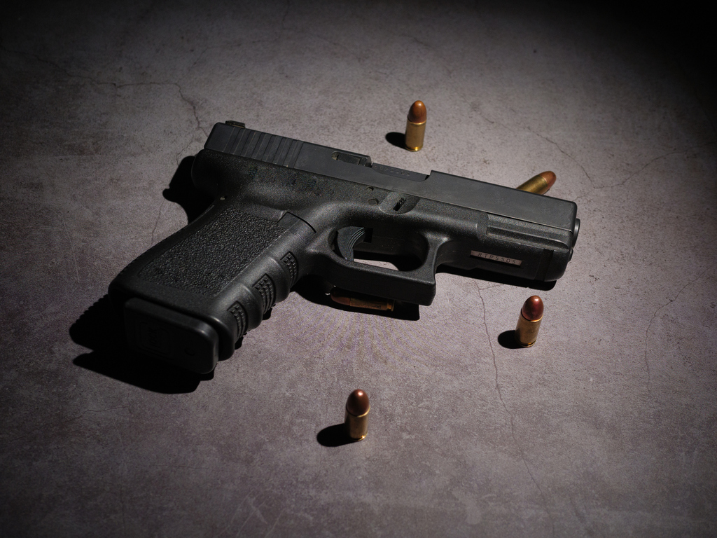 Close-up of a black metal 9mm automatic pistol with bullets all placed on a cement table with a black background. (iSock photo)