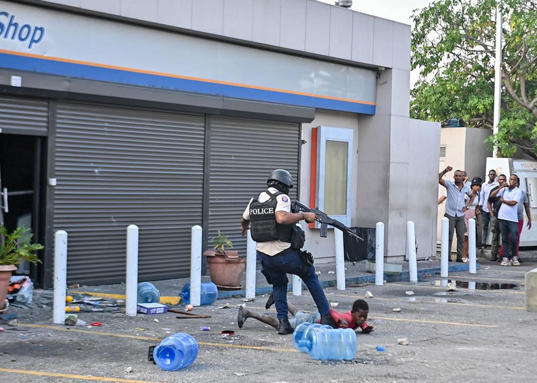 Un policier haïtien donne un coup de pied à un enfant lors d'une manifestation à Port-au-Prince le 6 février 2024, où des gens pillaient une épicerie. Le gouvernement haïtien a annoncé le 5 février 2024 une répression contre la Brigade de Sécurité des Aires Protégées (BSAP), accusée de violents affrontements avec la police la semaine dernière.
Richard PIERRIN / AFP