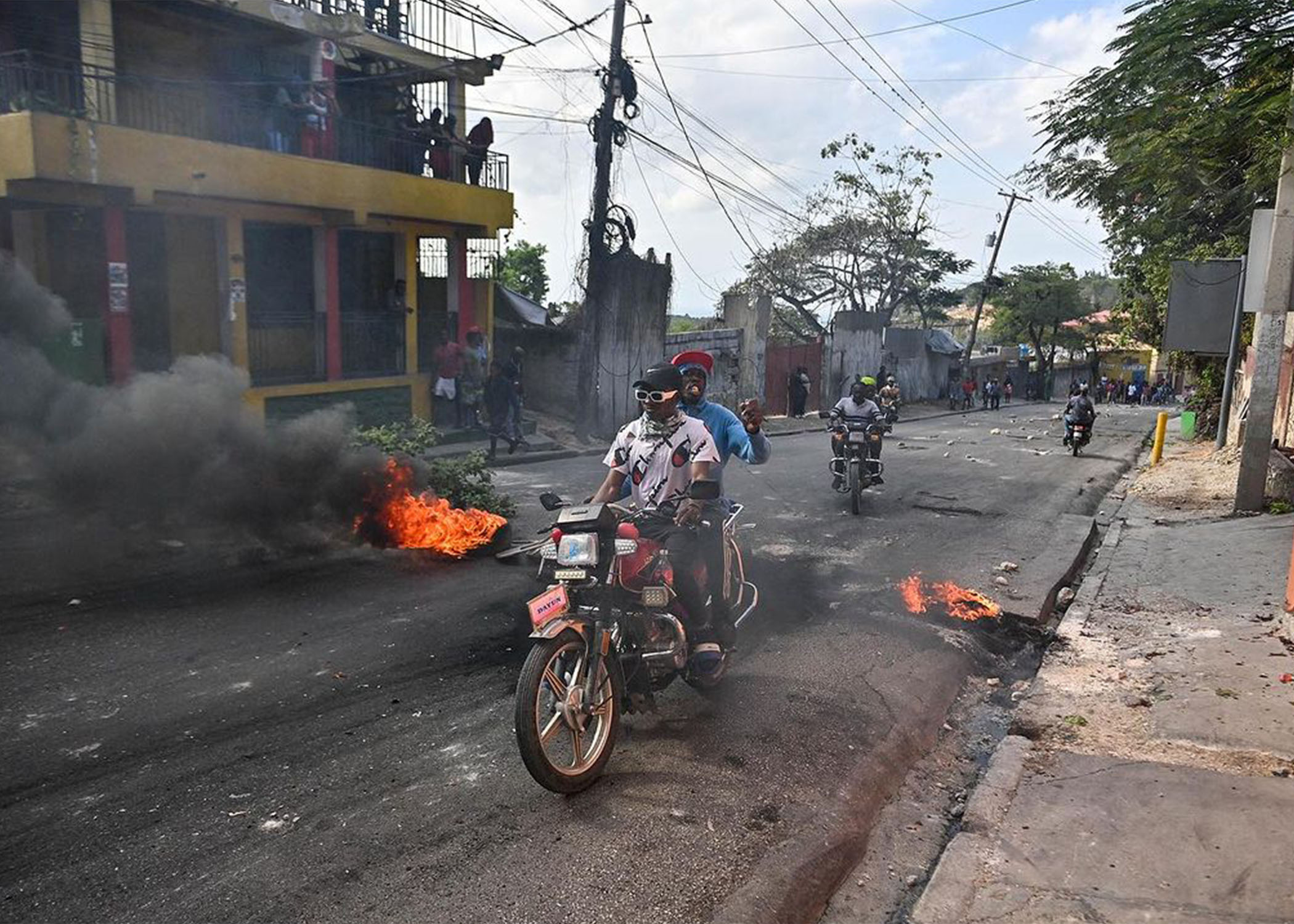 Des gens circulent à côté de pneus en feu lors d'une manifestation réclamant le départ du Premier ministre haïtien Ariel Henry à Port-au-Prince le 6 février 2024. Le gouvernement haïtien a annoncé le 5 février 2024 une répression contre la Brigade de Sécurité des Aires Protégées (BSAP), accusée d'affrontements violents avec la police la semaine dernière et dont les agents fortement armés ont récemment accru leur pouvoir. Richard PIERRIN / AFP